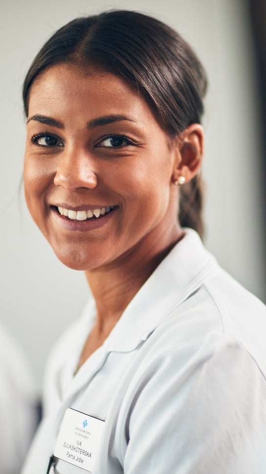 En kvinna i vit personalklädsel ler mot kameran.