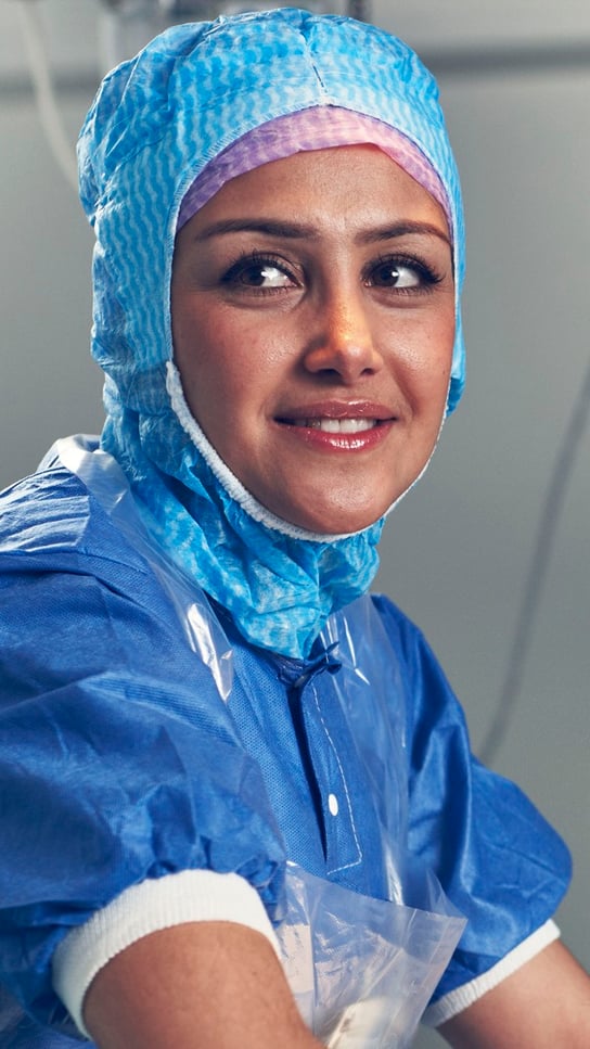 En kvinna i operationskläder ler mot kameran.