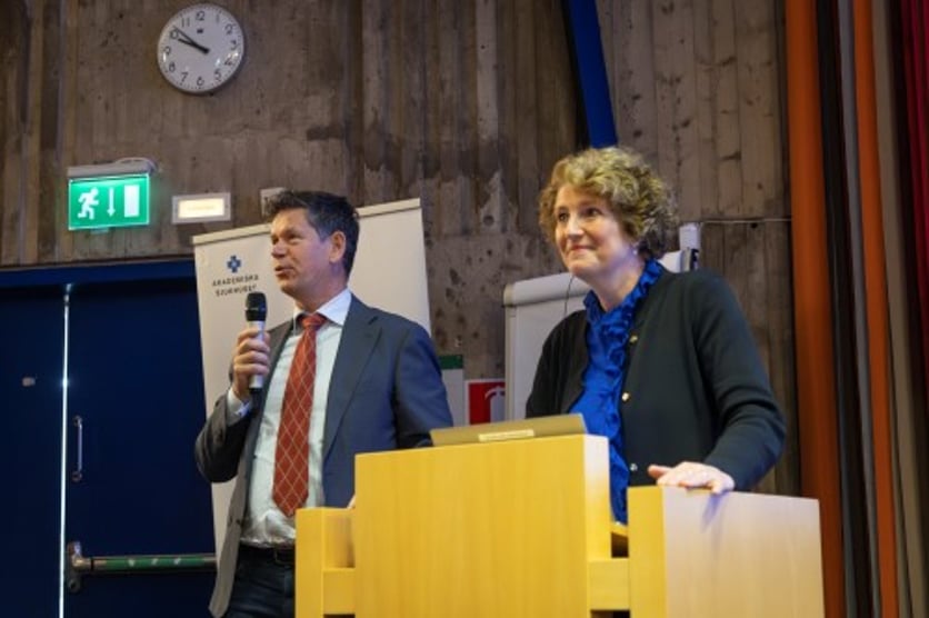 Man talar i mikrofon och kvinna står bredvid vid podium