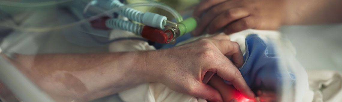 Två sjukvårdspersonal hanterar ett nyfött barn i kuvös