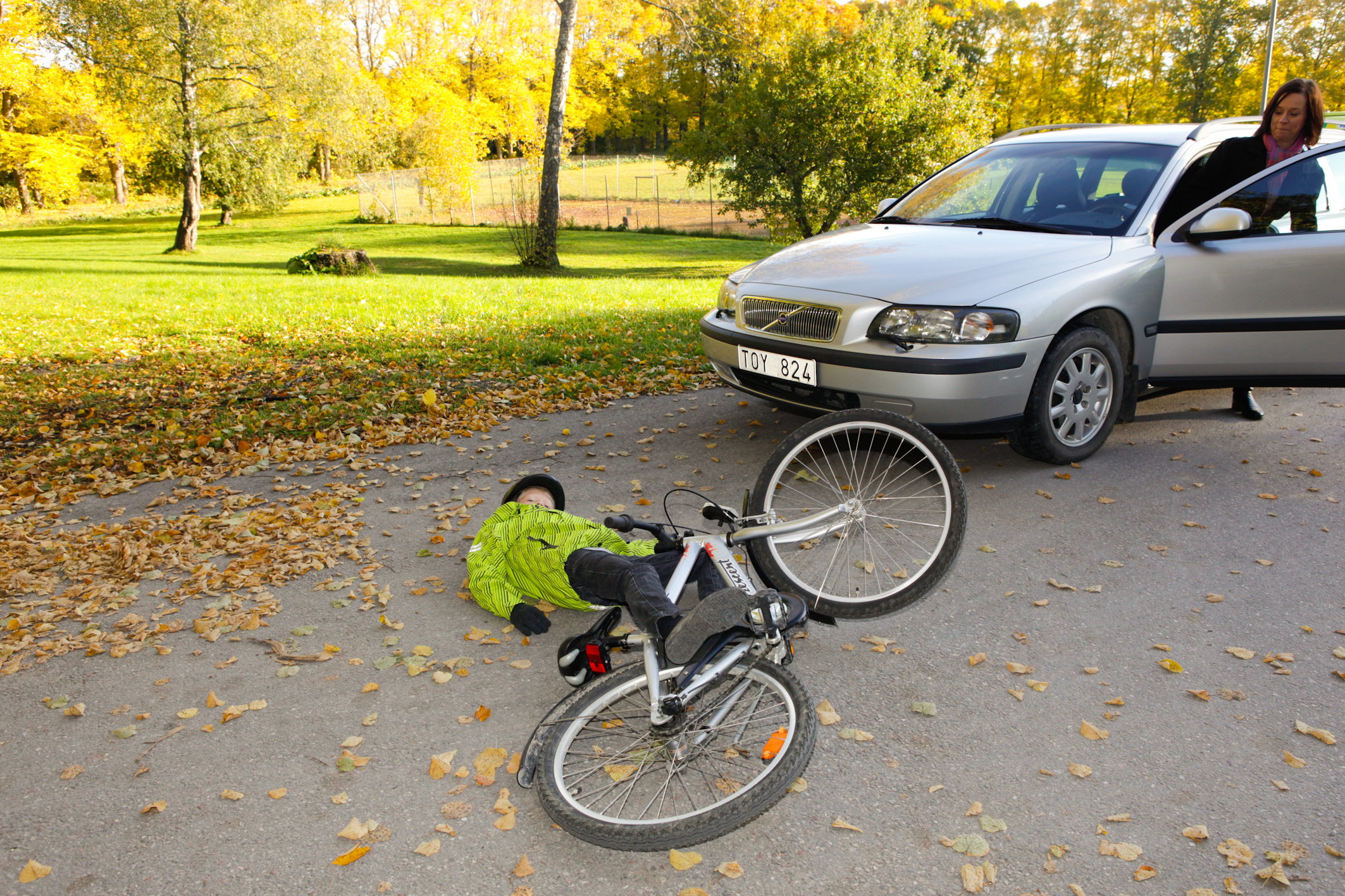 Pojke har krockat med bil och ligger på marken med cykel bredvid sig.