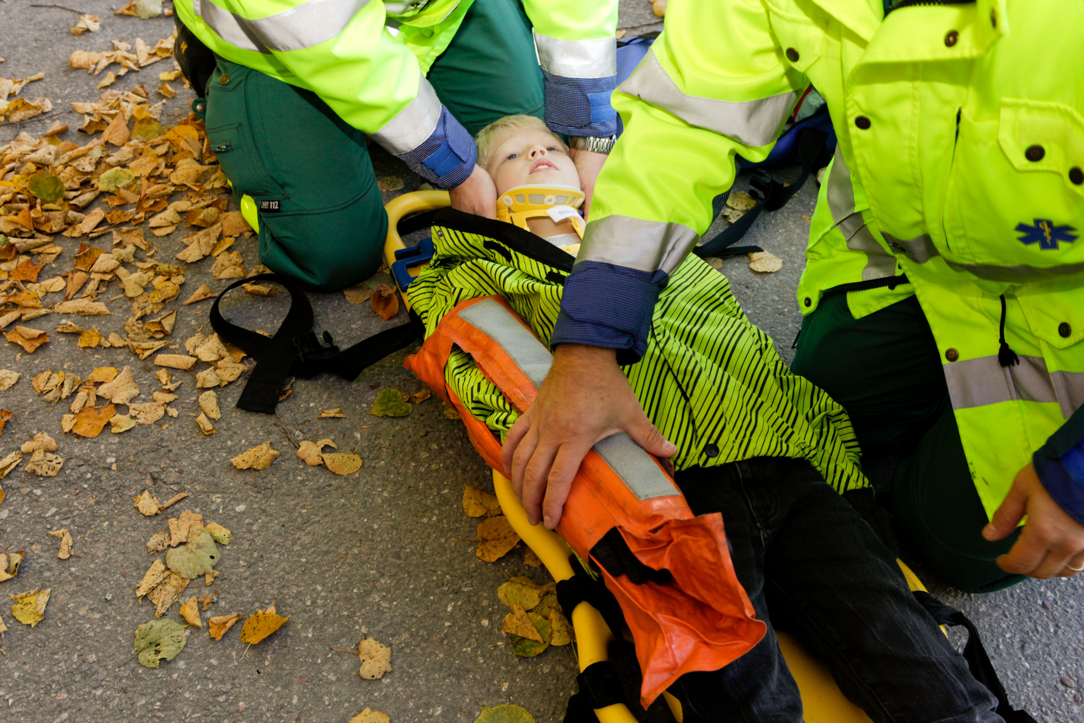 Pojke ligger på spineboard med nackkudde och vacuumkudde på armen.