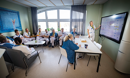 Många personer sitter i ett rum och tittar på en storbildsskärm