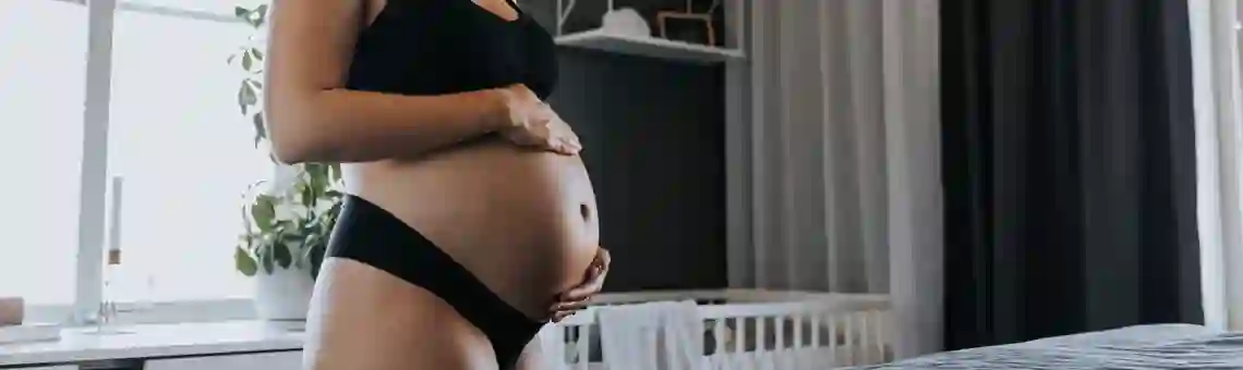 En gravid kvinna står vid sin säng
