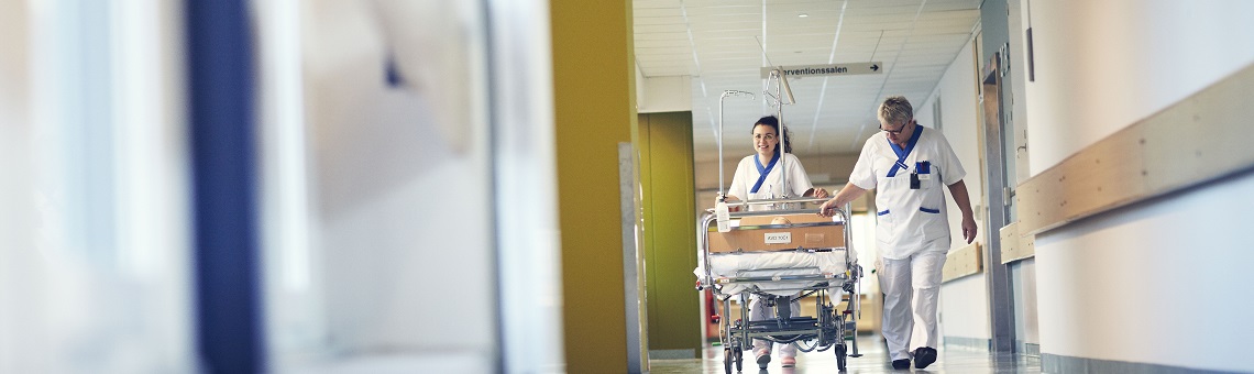 Caregivers walk with bed in corridor.