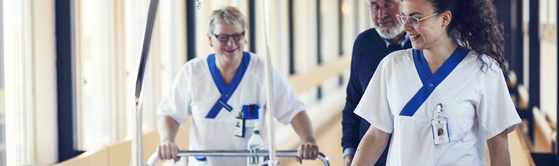 Kvinnlig sjukvårdspersonal går med patientsäng i korridor.